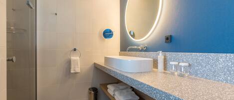 Un baño moderno con cabina de ducha de vidrio, un lavabo blanco, un espejo con luz y un perchero para toallas.