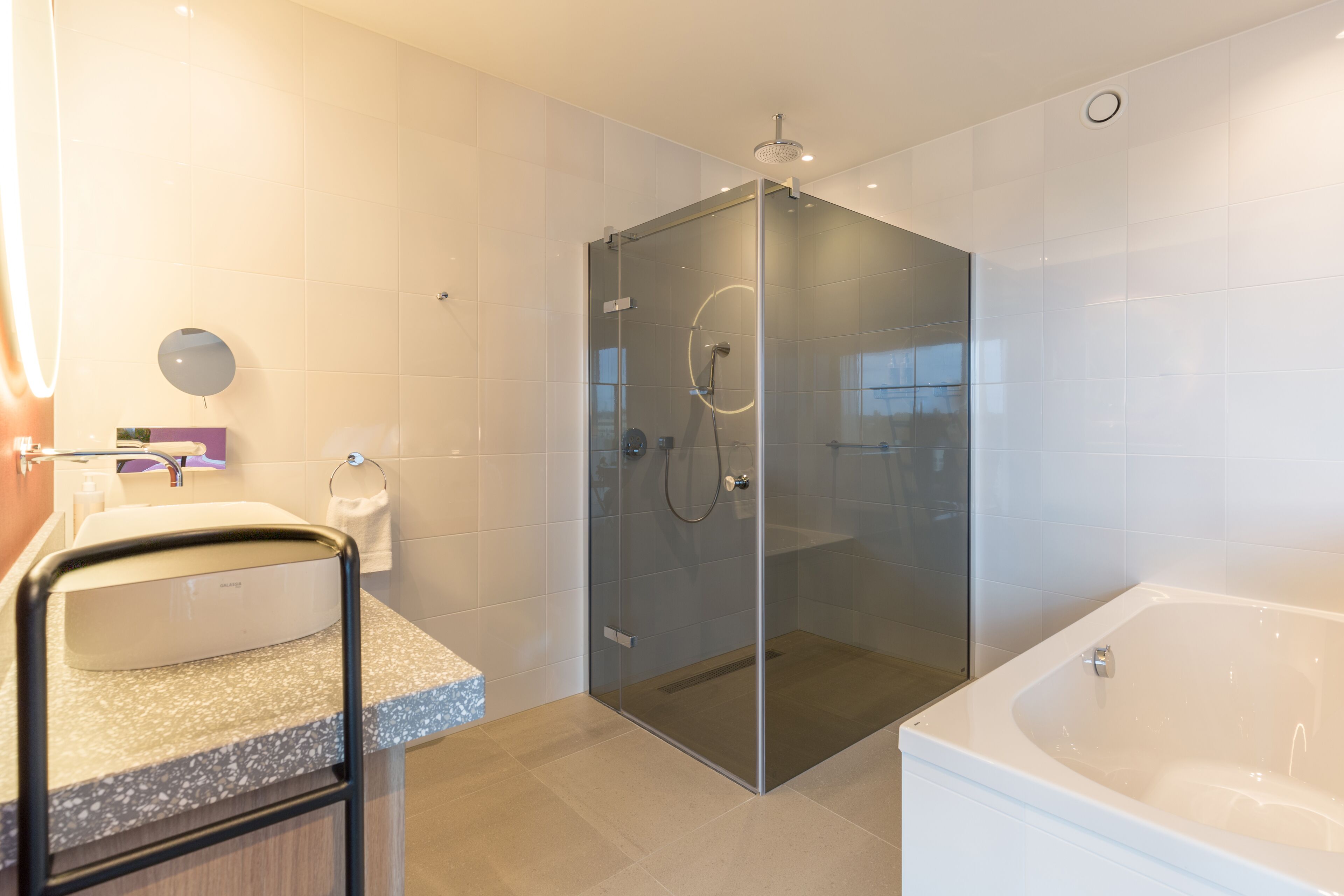 Een moderne badkamer met een douchecabine van glas, een vrijstaand bad en een wastafel met zeepdispenser.