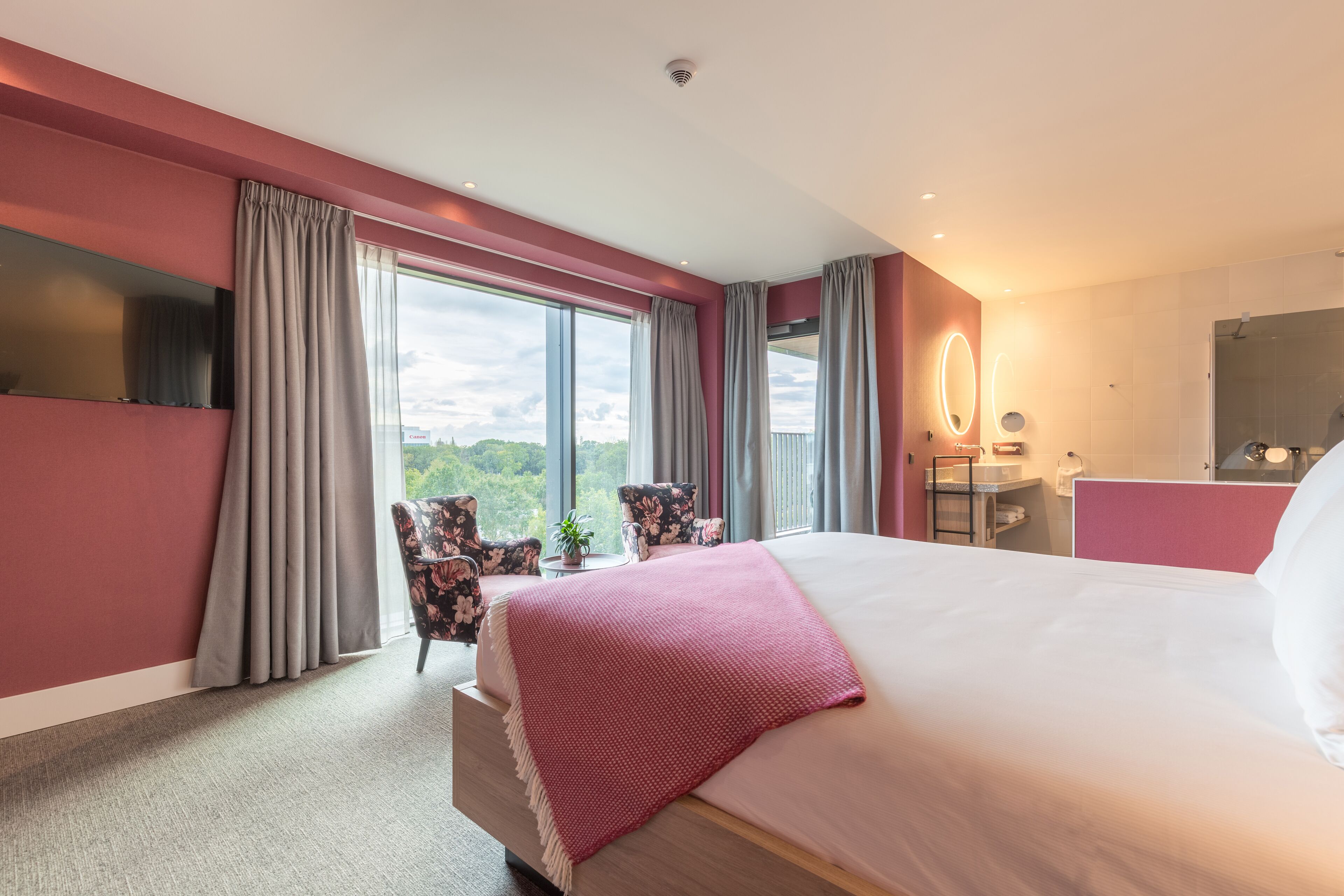 Une chambre d’hôtel moderne, dotée d’un grand lit, d’un bureau, d’une chaise et offrant une vue sur l’extérieur.