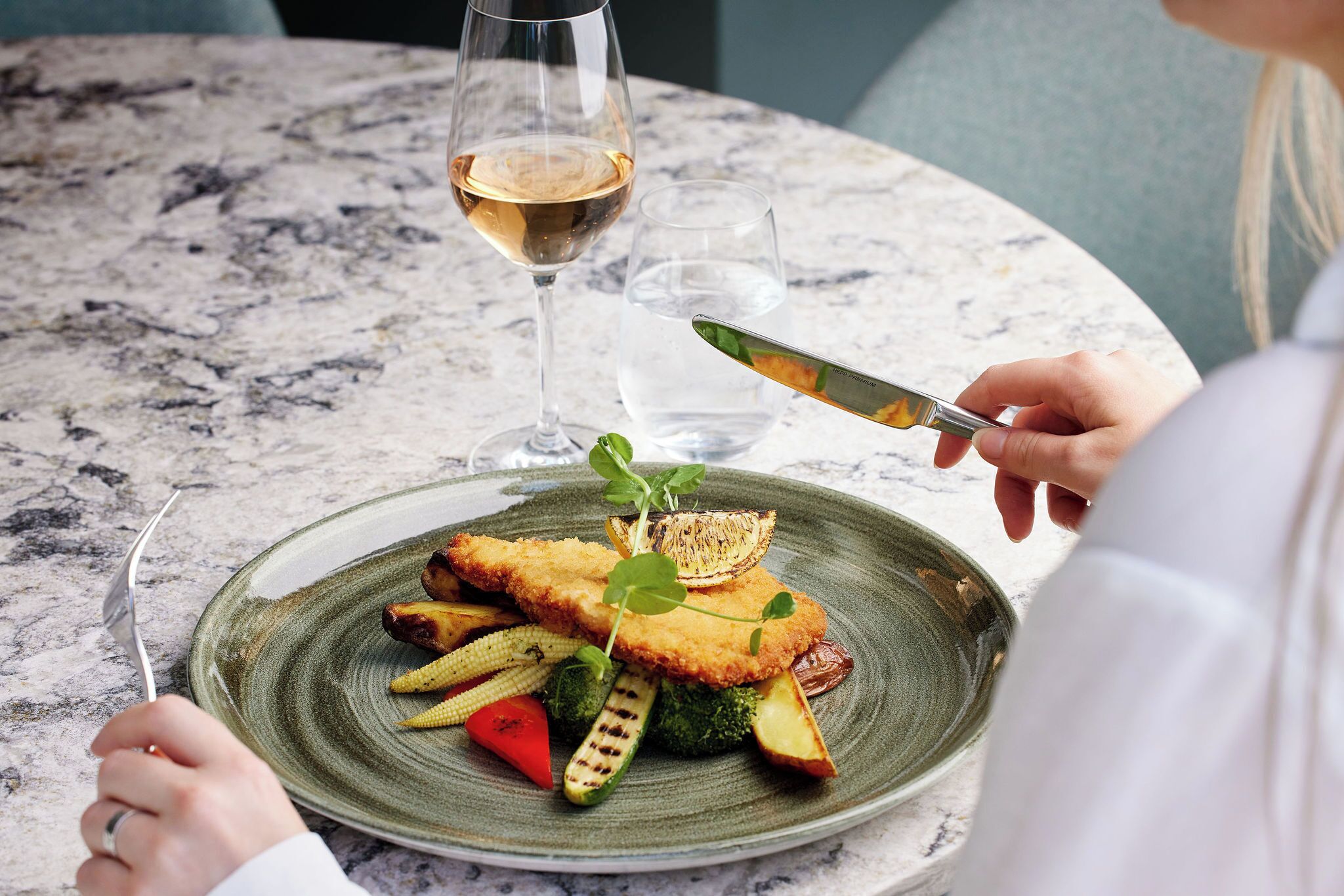 Une assiette de nourriture accompagnée d’un verre de vin blanc, le tout posé sur une table en marbre.