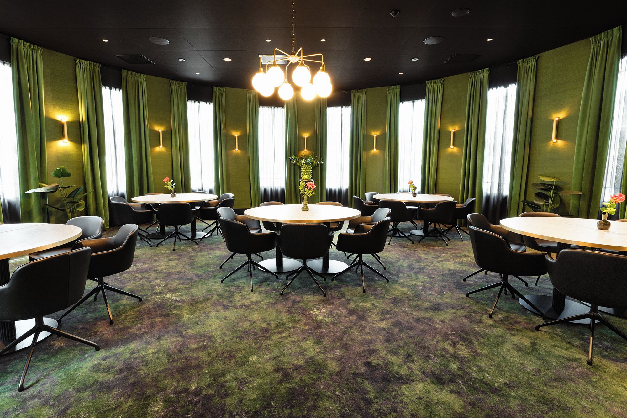 Un salón de conferencias con mesas redondas y sillas, cortinas verdes y un candelabro.