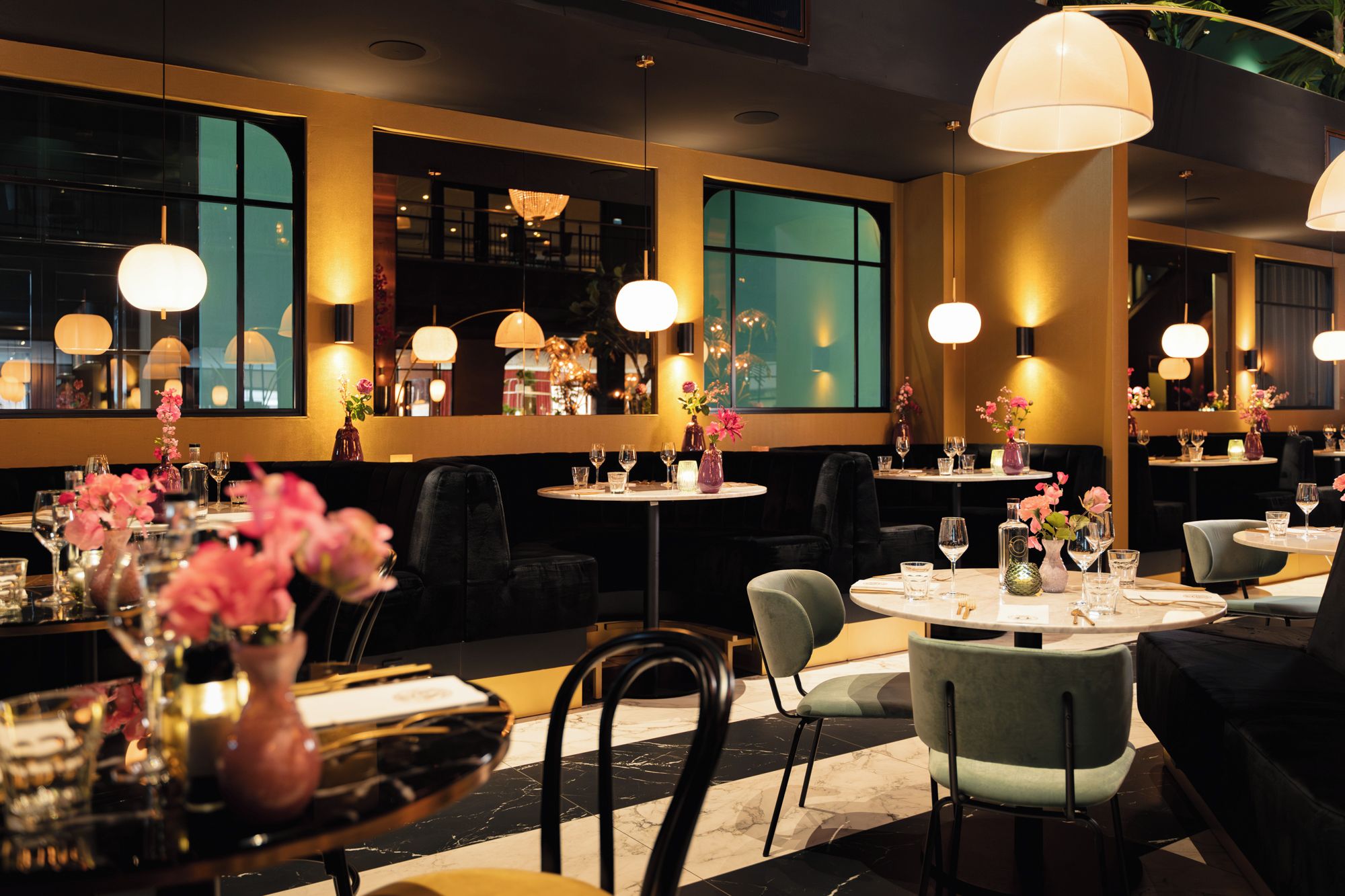 Een restaurantinterieur met ronde tafels, stoelen en hangende lampen.