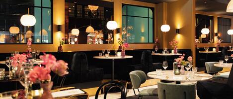 Un interior de restaurante con mesas redondas, sillas y lámparas colgantes.