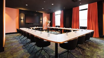 Une salle de conférence avec une longue table, des chaises noires, un téléviseur à écran plat et des rideaux rouges.