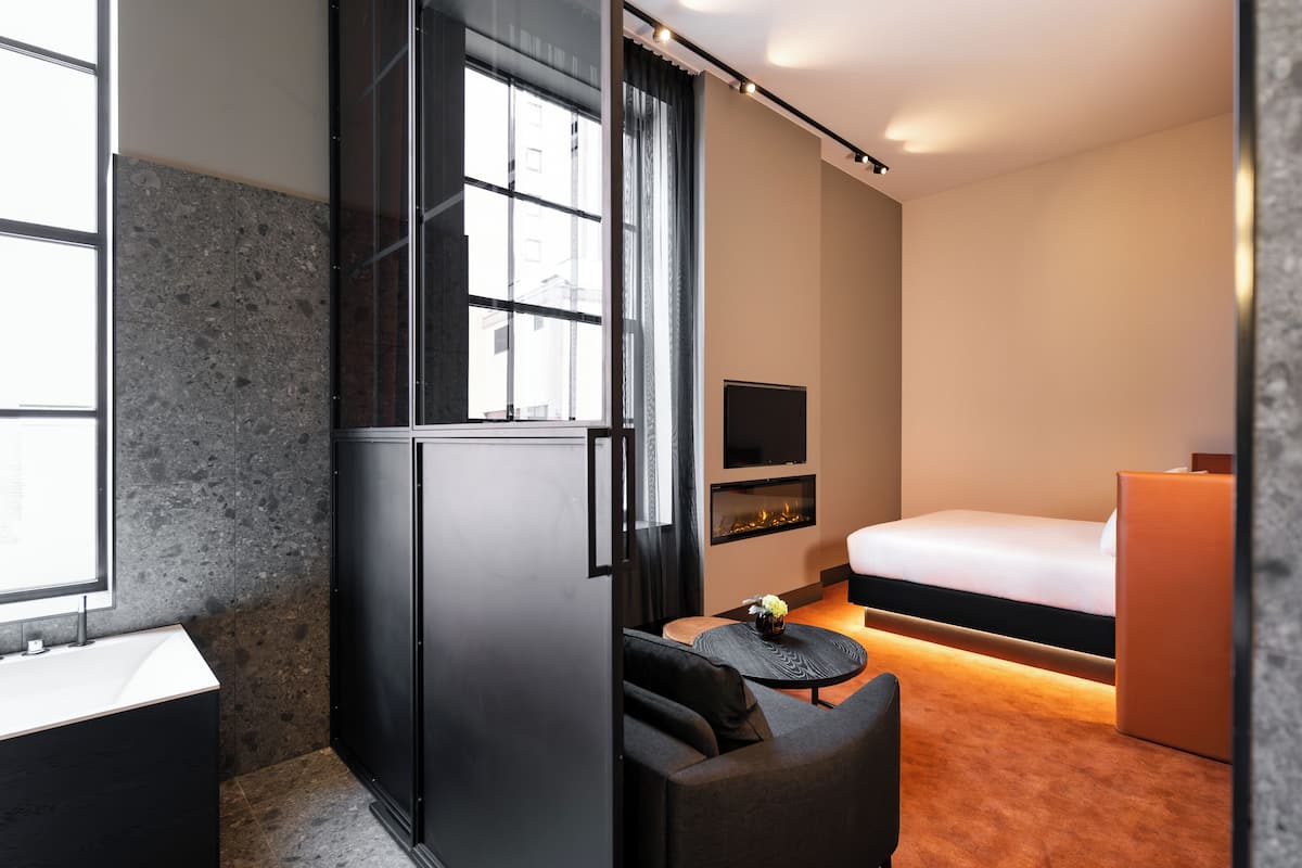 Ein modernes Hotelzimmer mit großem Fenster, einem Flachbildfernseher, einem Bett, einem Sofa und einem kleinen Tisch mit einer Vase.