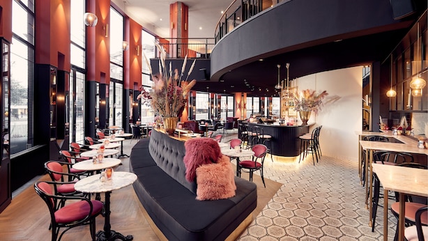 A modern interior with a black sofa, round tables, and red chairs. - Theaterhotel De Oranjerie (Roermond)