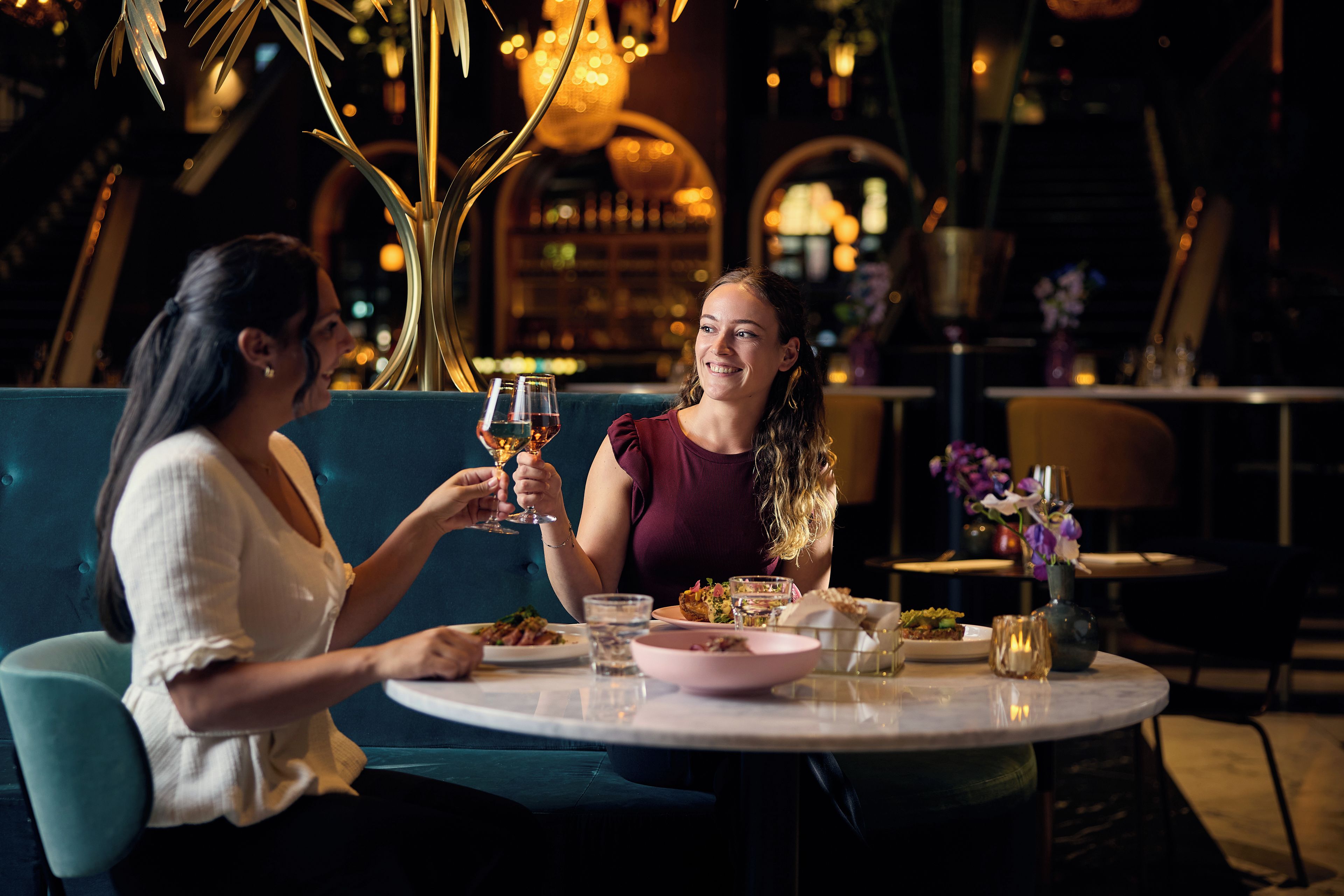 Two people seated at a round table with a bottle of wine, a glass of water, and a plate of food.