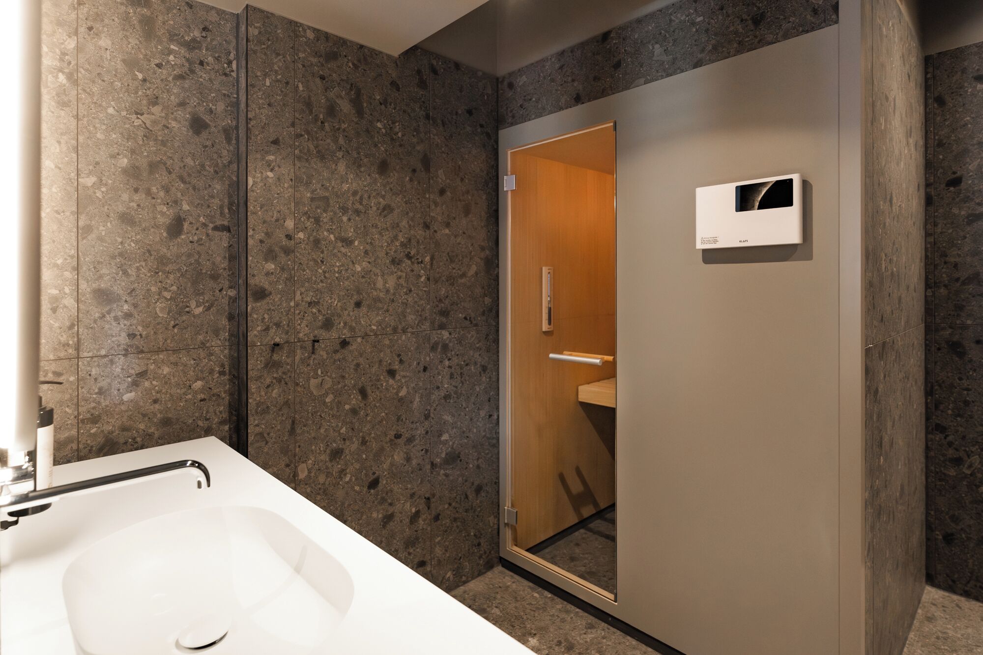 A modern bathroom with a large sink, dark speckled walls, and a mirror with a wooden door.