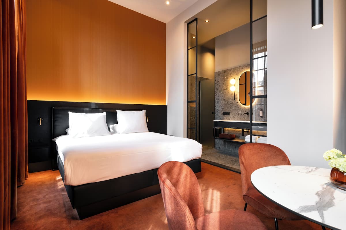 Ein modernes Hotelzimmer mit einem großen Bett, einer Sitzecke mit Tisch und Blick auf die Stadt durch eine Glaswand.