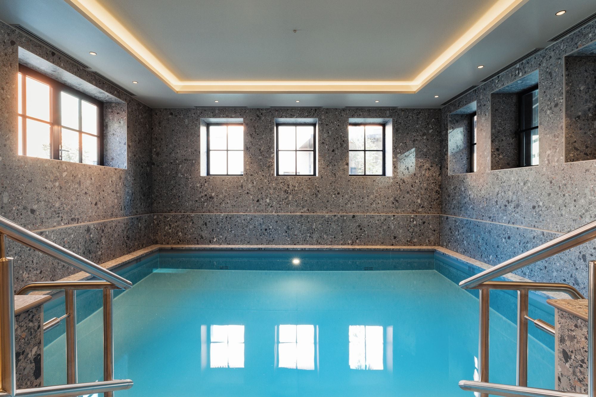 Une piscine à l ’eau d’un bleu limpide, entourée de murs à motifs pointillés.
