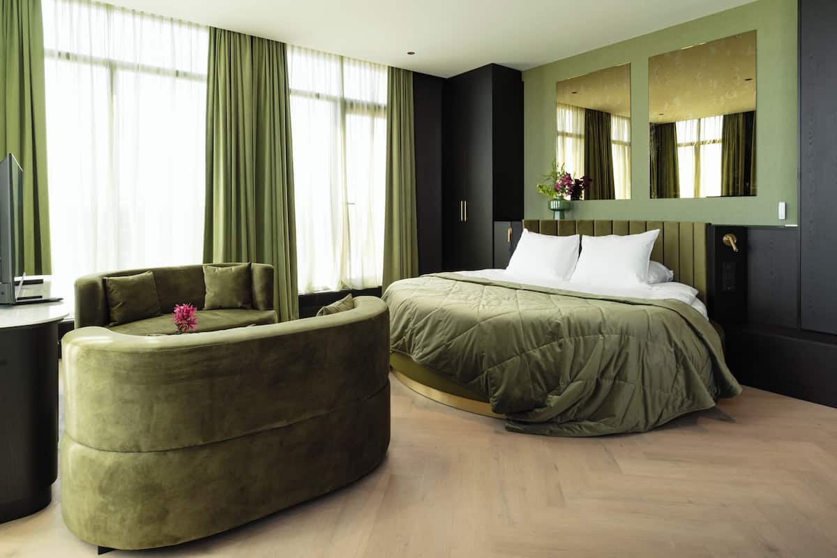 Ein modernes Hotelzimmer mit einem großen Bett, einer Couch, einem Schreibtisch mit einem Laptop und einem großen Spiegel.