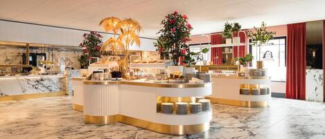 A modern hotel lobby with marble flooring, a central reception desk, and decorative plants.
