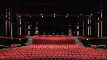 A theater with rows of red seats, a central stage, and a dark interior.