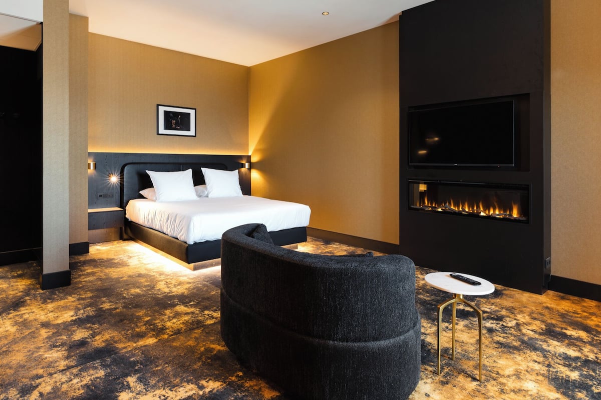 Ein modernes Hotelzimmer mit einem großen Bett, einem wandmontierten Fernseher und einem Kamin.