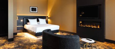 A modern hotel room with a large bed, a wall-mounted TV, and a fireplace.