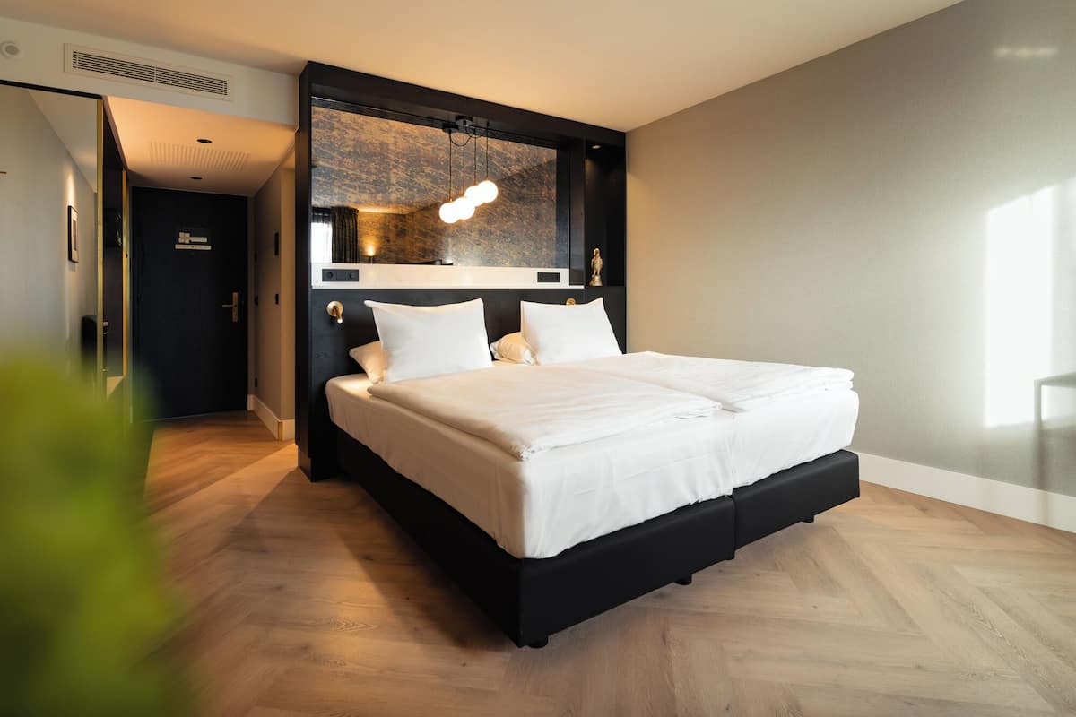 Ein modernes Hotelzimmer mit einem großen Bett, einem dunklen Kopfteil und einem einzigartigen Wandbild darüber.