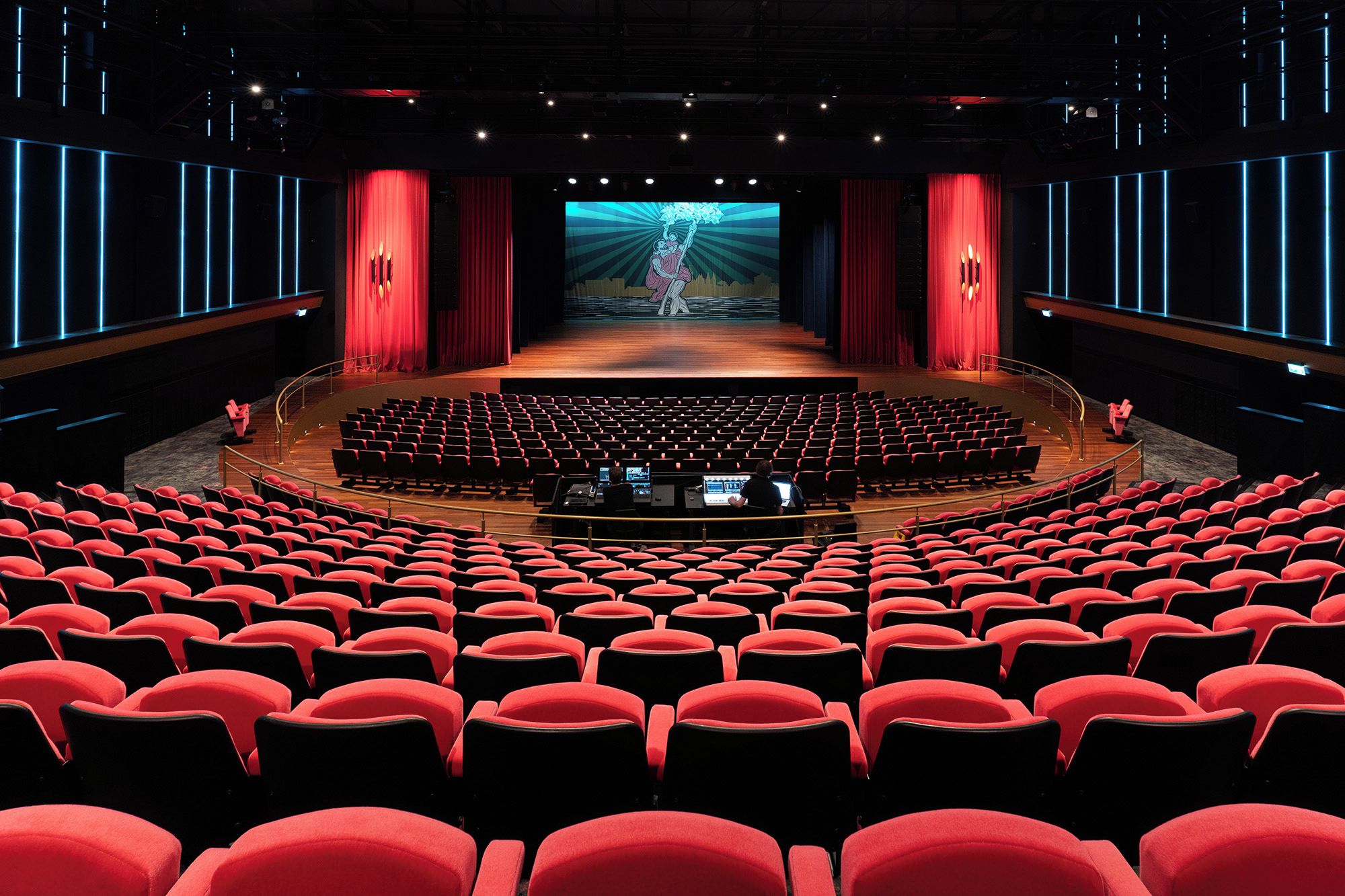 A theater with a central stage, red curtains, and rows of red seats.