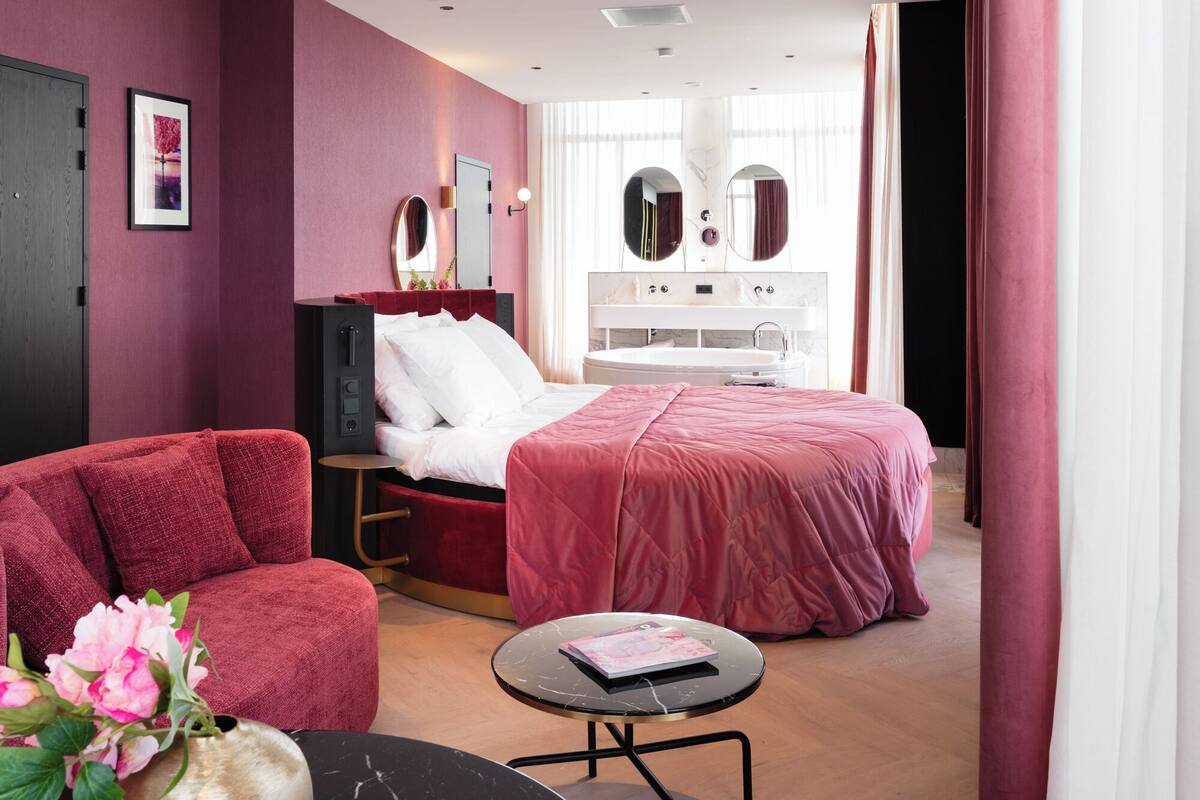 Ein modernes Schlafzimmer mit einem Bett, einem Schminktisch mit Spiegel, einem kleinen runden Tisch und einem roten Sessel.