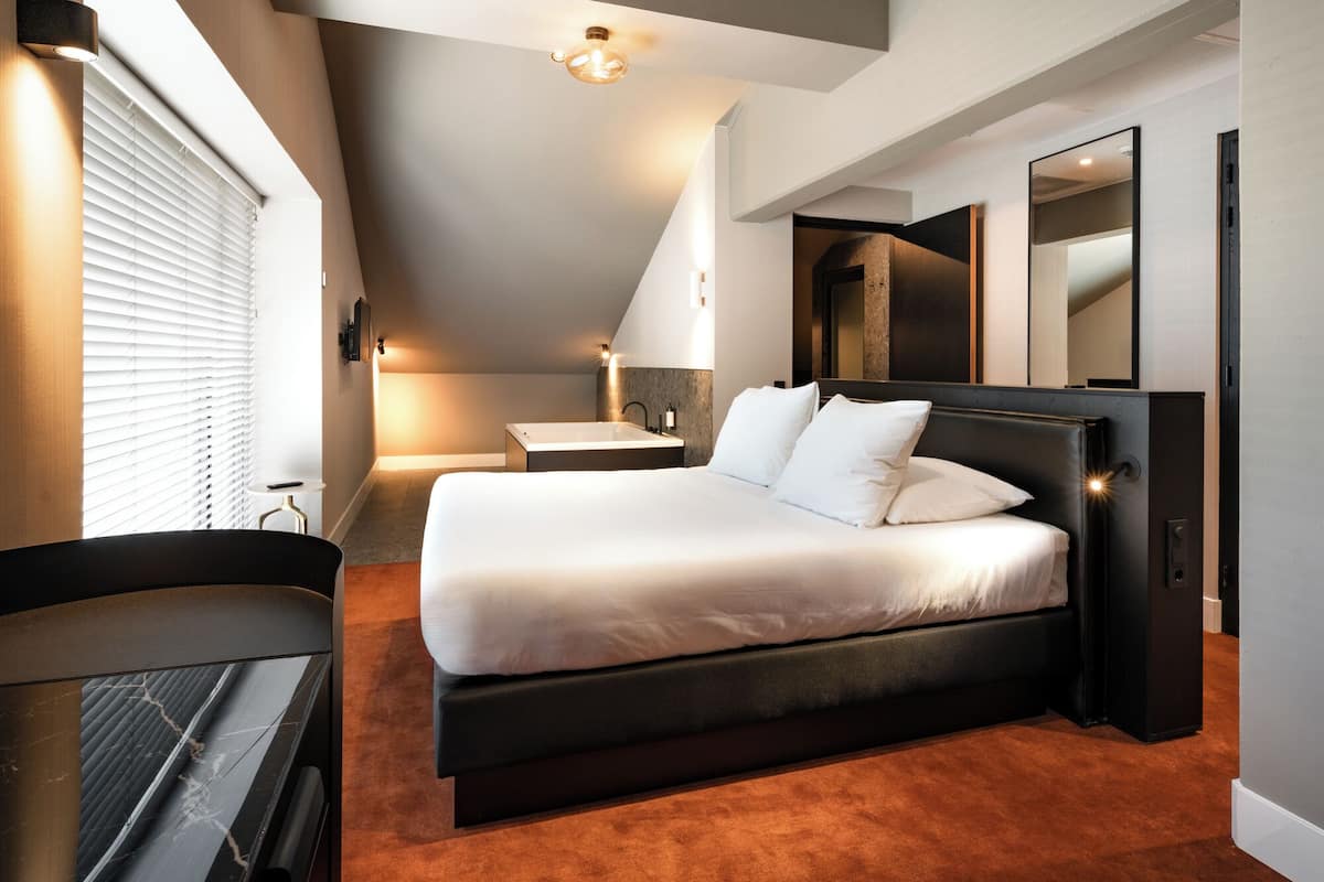 Ein modernes Schlafzimmer mit einem großen Bett, einem fest eingebauten Schreibtisch und einem Badezimmer mit Badewanne.