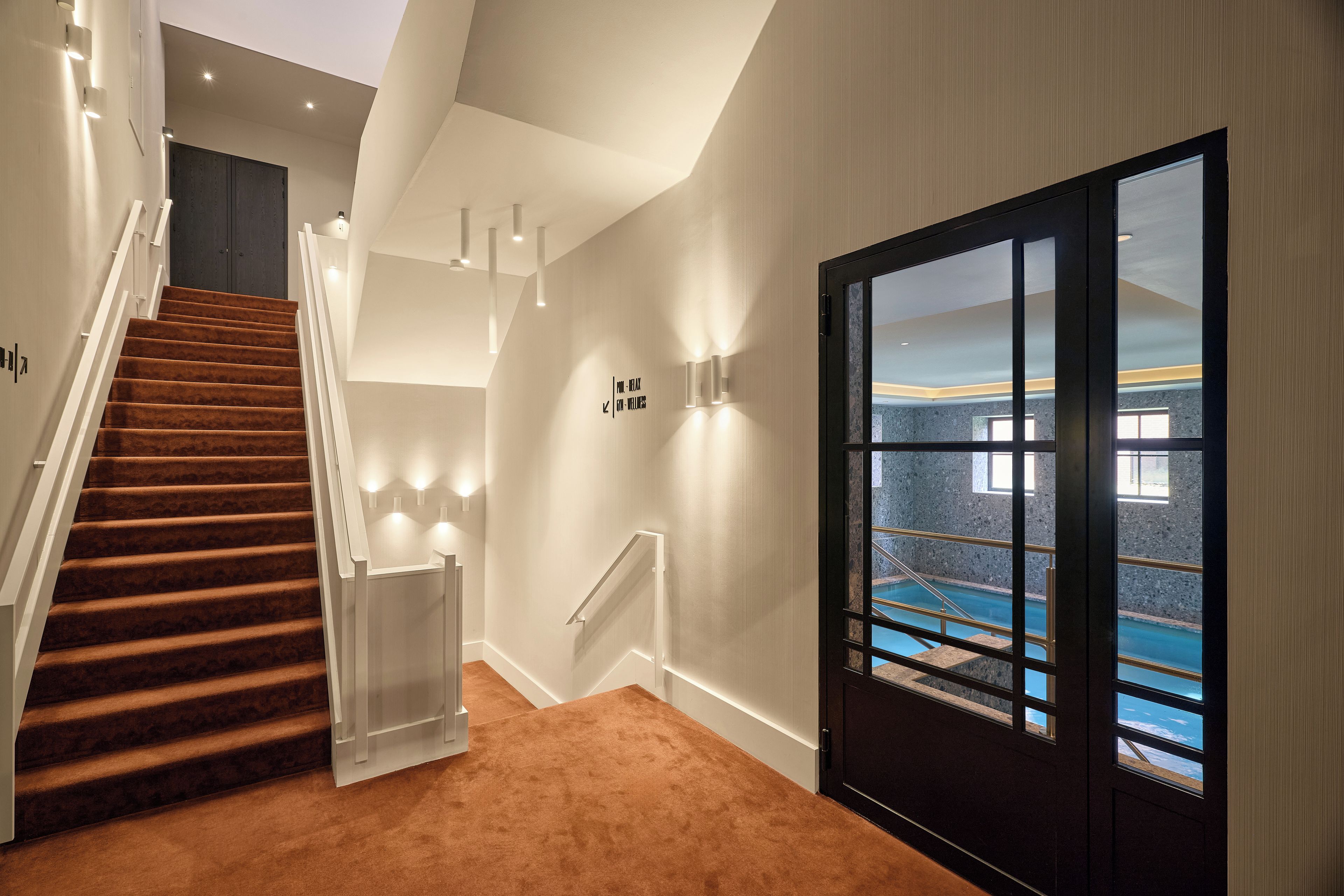 A modern interior with a staircase, a glass door leading to a pool area, and a sign indicating a wellness area.