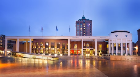 Un hotel con una entrada imponente, varias banderas y un edificio destacado al fondo.