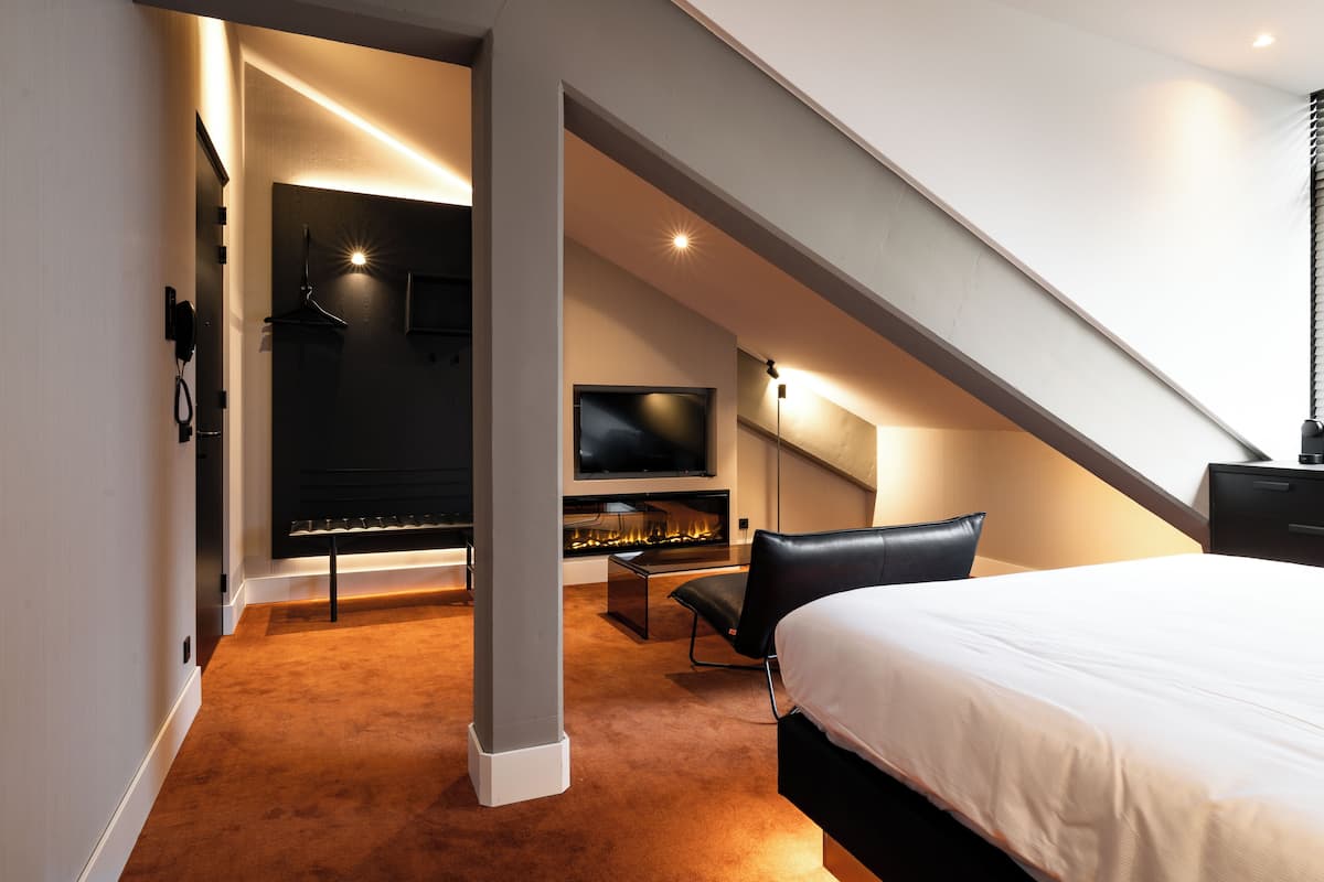 Ein modernes Hotelzimmer mit einem großen Bett, einem Flachbildfernseher, einem Kamin und einer Sitzecke mit Sessel und Tisch.