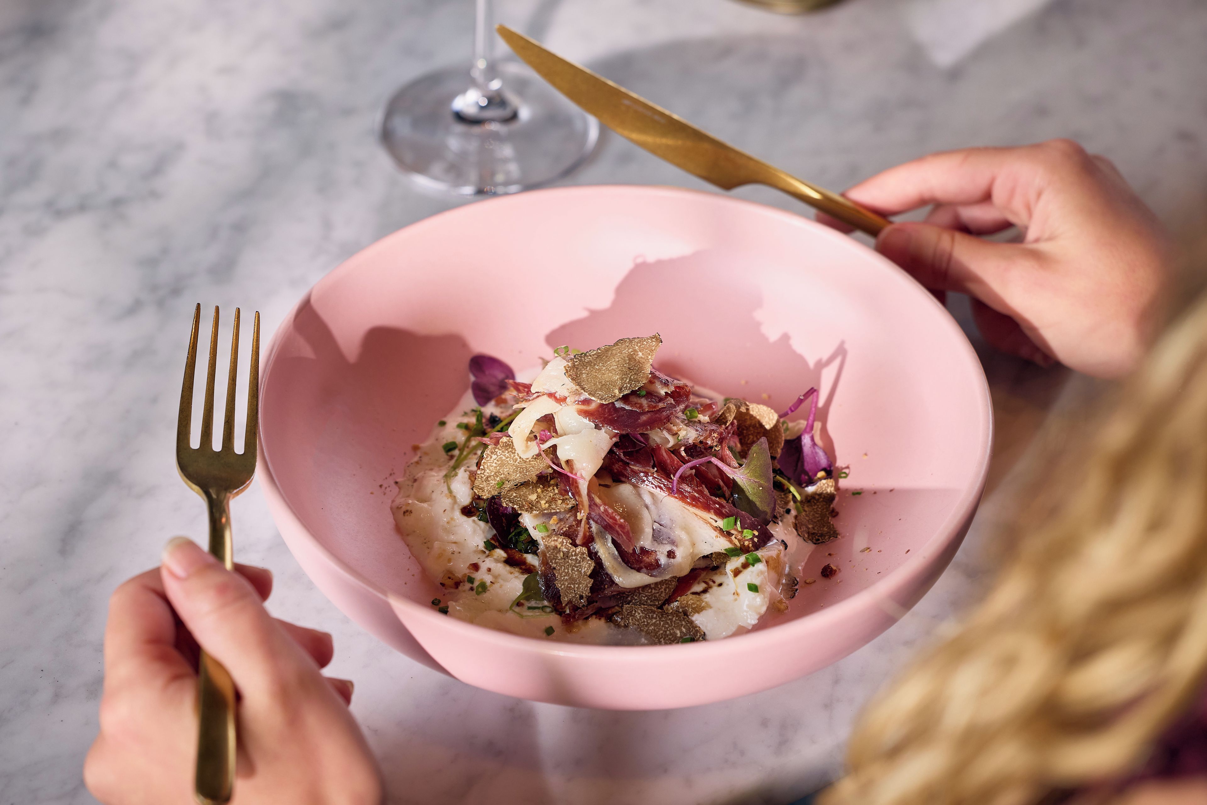 A pink bowl with a variety of food items on a marble surface.