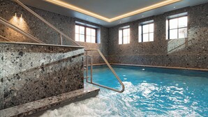 An indoor swimming pool with a stone wall, a metal ladder, and windows. - Theaterhotel De Oranjerie (Roermond)