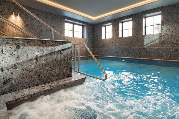 Ein Hallenbad mit Steinwand, Metallleiter und Fenstern.