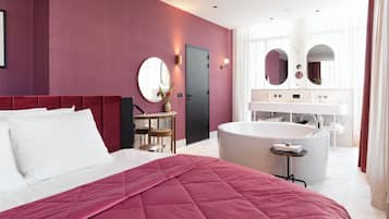 Une chambre d’hôtel moderne dotée d’un grand lit, d’un coin salon avec une table et des chaises, d’une grande baignoire et d’une salle de bain avec un meuble-lavabo et des miroirs.