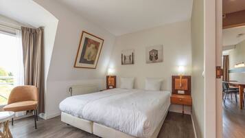 A hotel room with a large bed, a chair, a table, and artwork on the walls.
