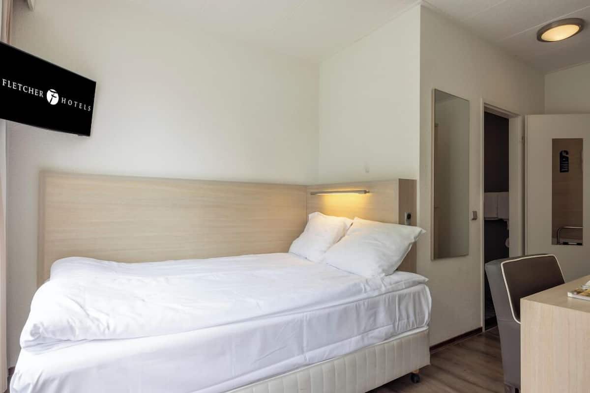 Hotellihuone, jossa on sänky, työpöytä, tuoli ja peili.