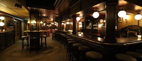 A bar area with multiple stools and a bar counter, featuring hanging light fixtures and a wooden interior.