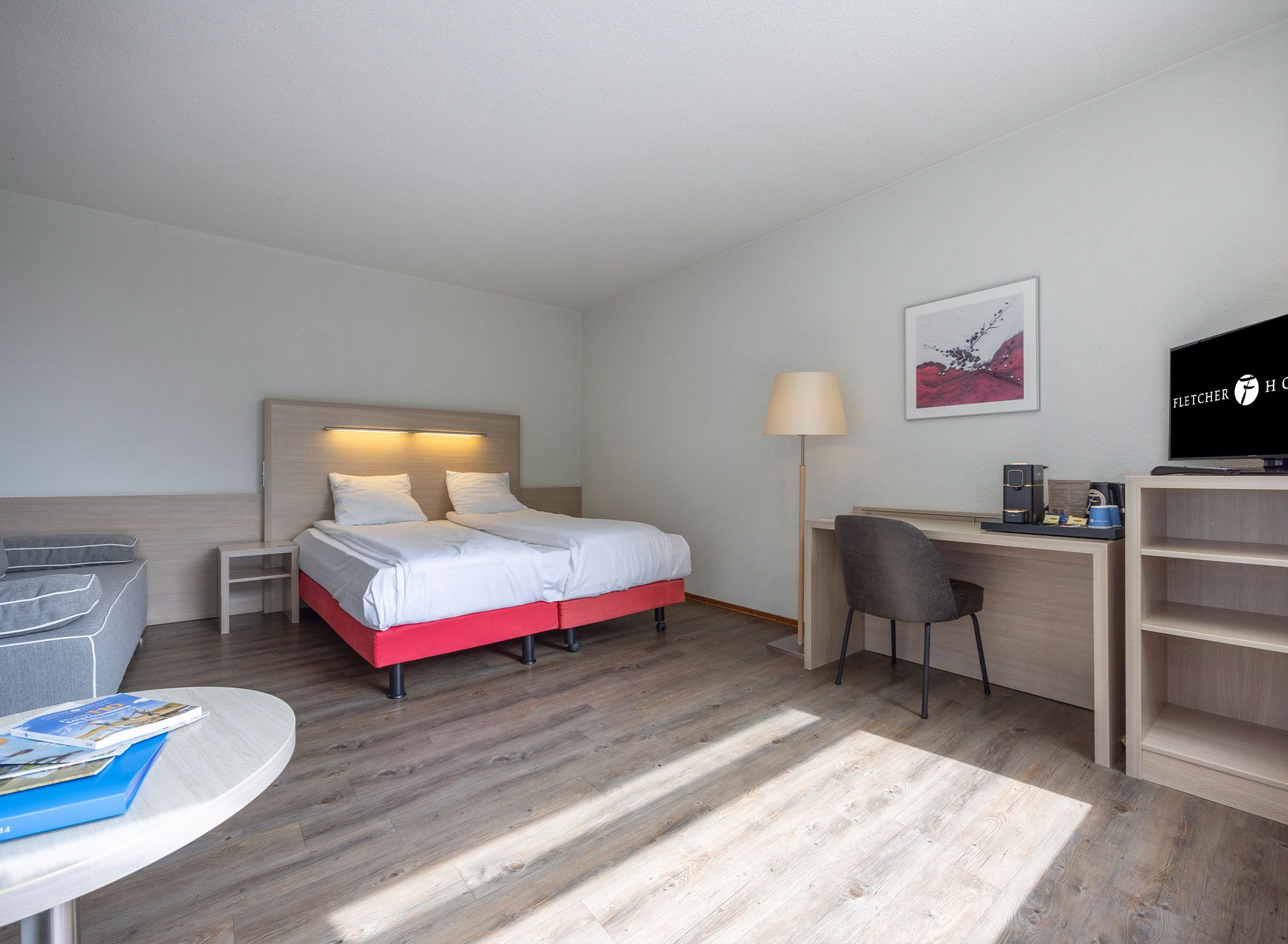 A hotel room with a bed, desk, chair, TV, and a lamp.