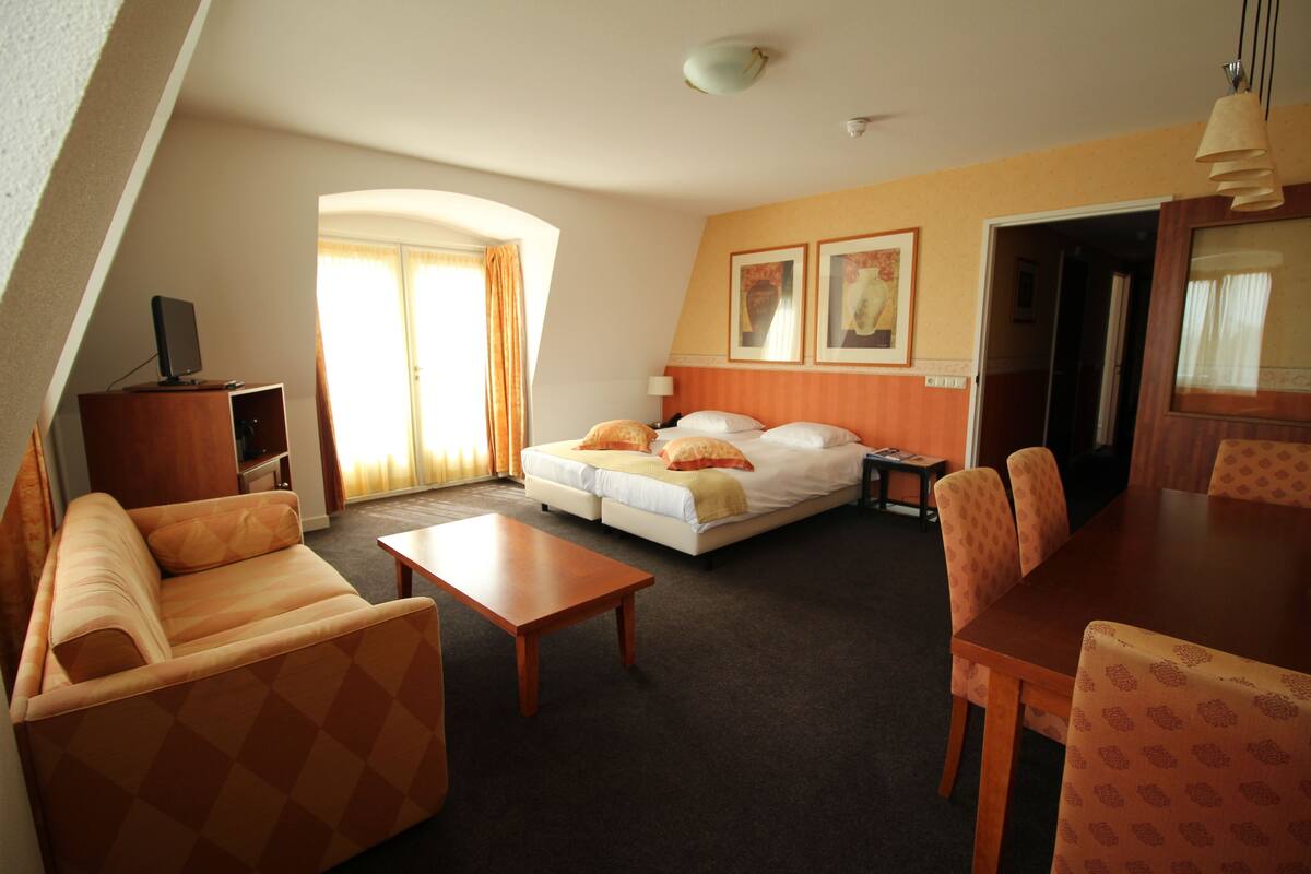 Hotellihuone, jossa on sohva, sänky, ruokapöytä ja televisio.