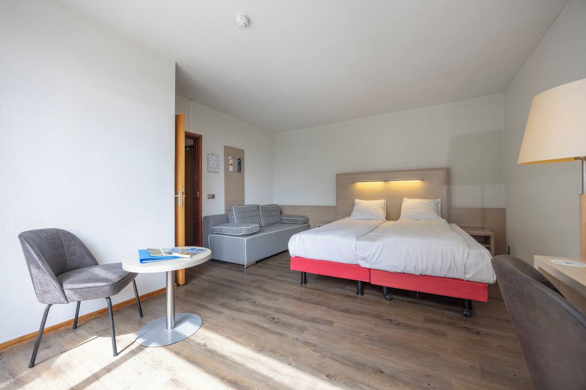 Hotellihuone, jossa on sänky, sohva, tuoli, pieni pöytä ja lamppu.