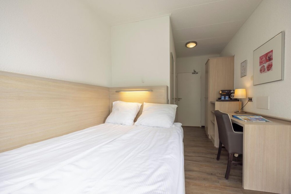 Et hotelværelse med en seng, et skrivebord og en stol.