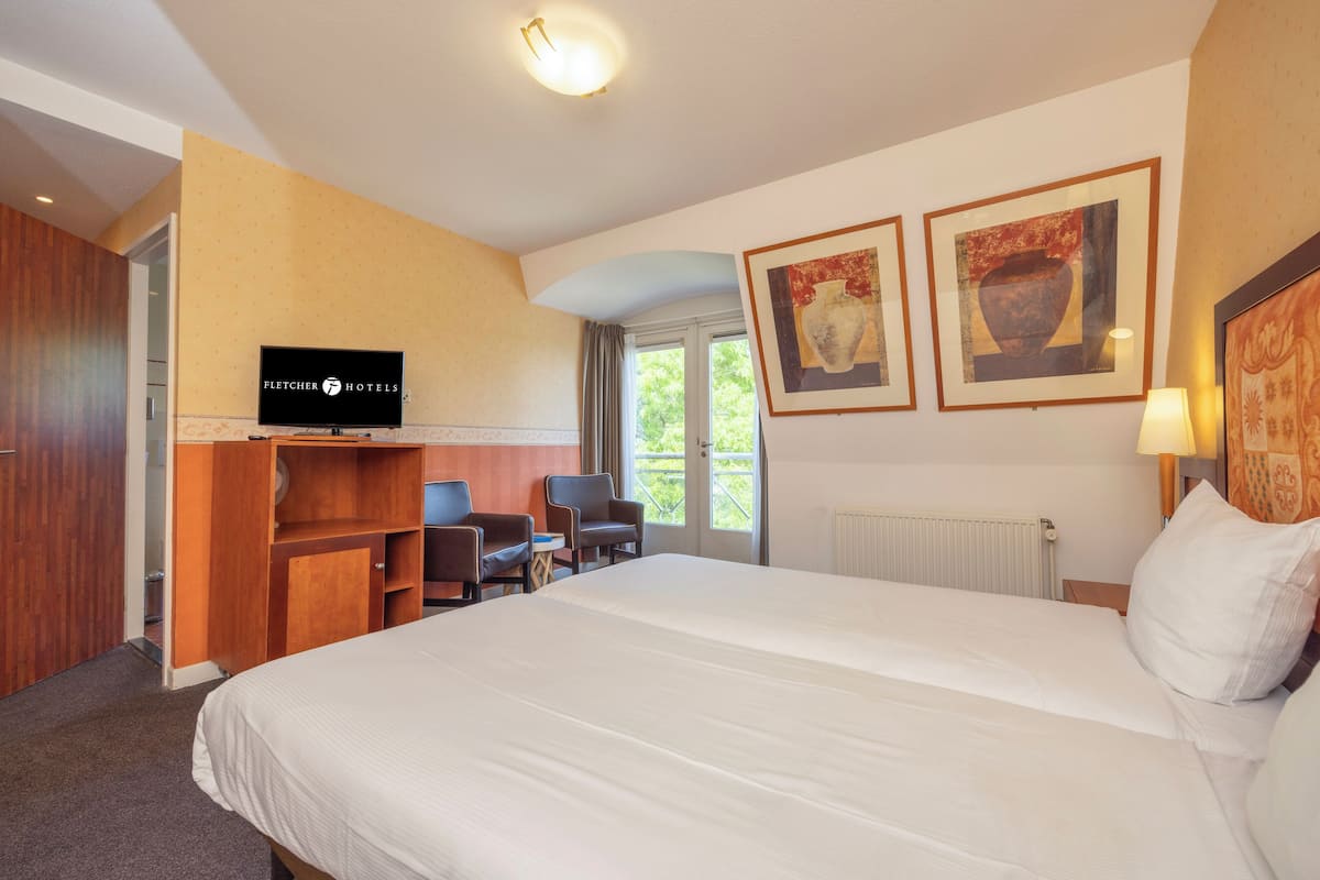 Hotellihuone, jossa on suuri sänky, televisio, työpöytä tuoleineen sekä taideteoksia seinillä.