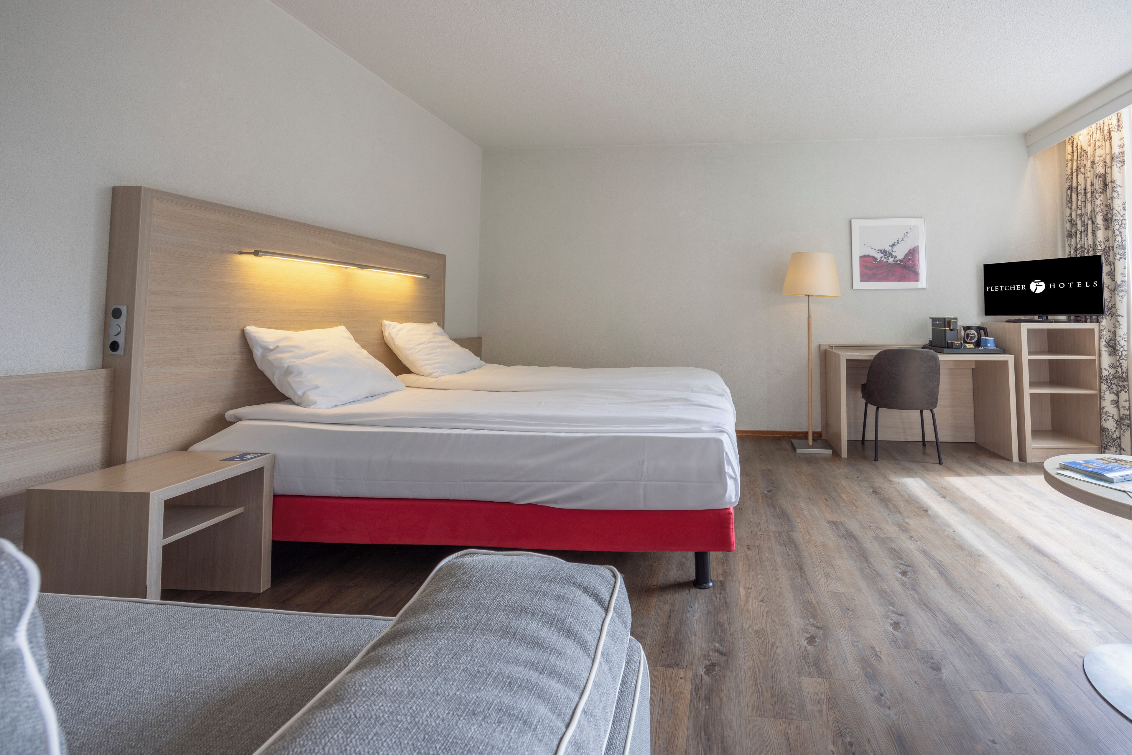 Et hotelværelse med seng, sengebord, lampe, fjernsyn og et skrivebord med stol.