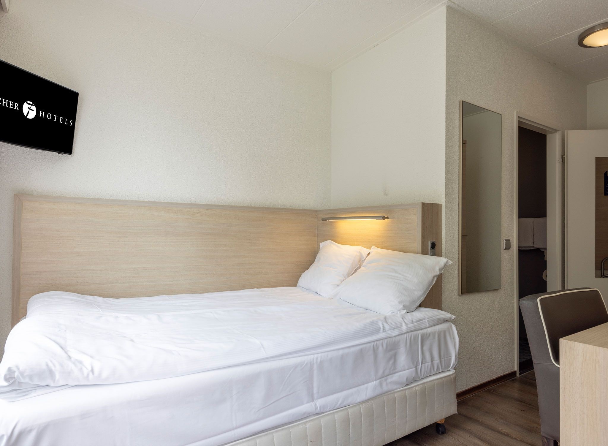 Una habitación de hotel con una cama, un escritorio y un televisor fijado a la pared.