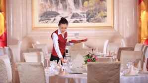 A dining area with tables set for a meal, a waiter serving a tray of glasses, and a painting of a waterfall on the wall. - XinHai JinJiang Hotel Wangfujing (Beijing)