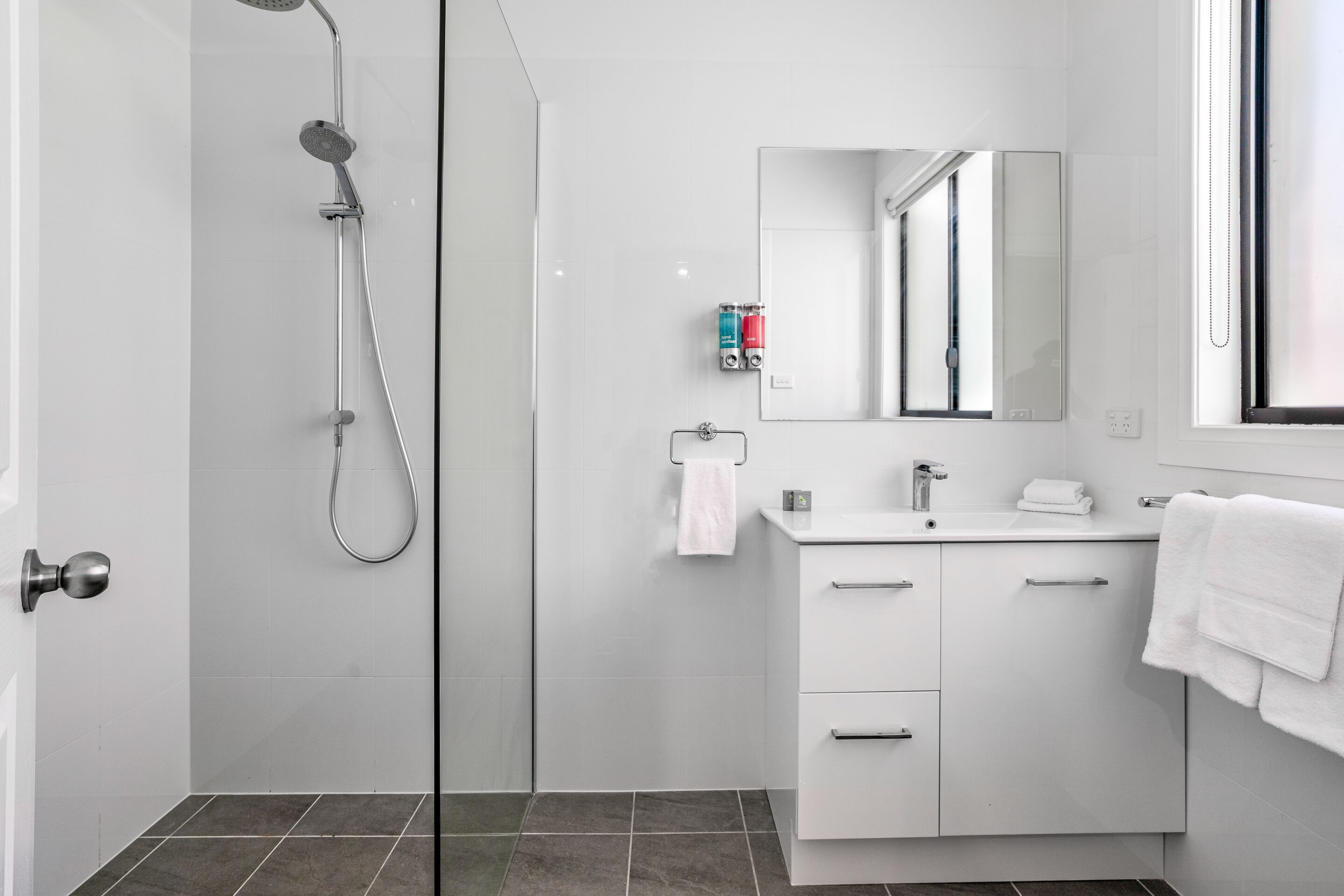 A modern bathroom with a glass shower enclosure, white vanity, and a large mirror.