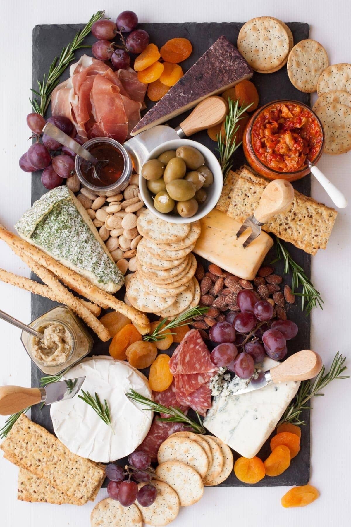 A charcuterie board with various cheeses, meats, olives, and crackers.