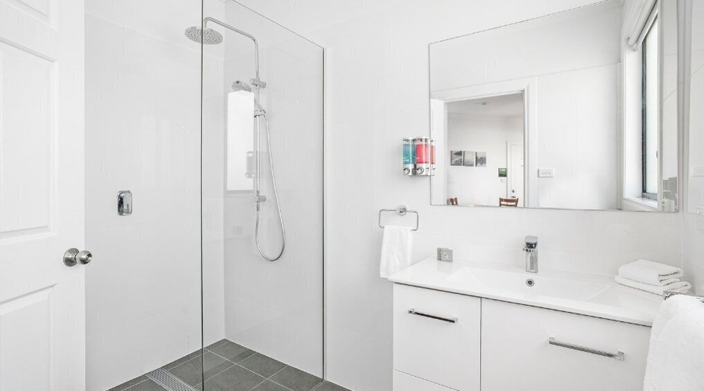 A modern bathroom with a glass-enclosed shower, a white sink with a mirror, and a tiled floor.