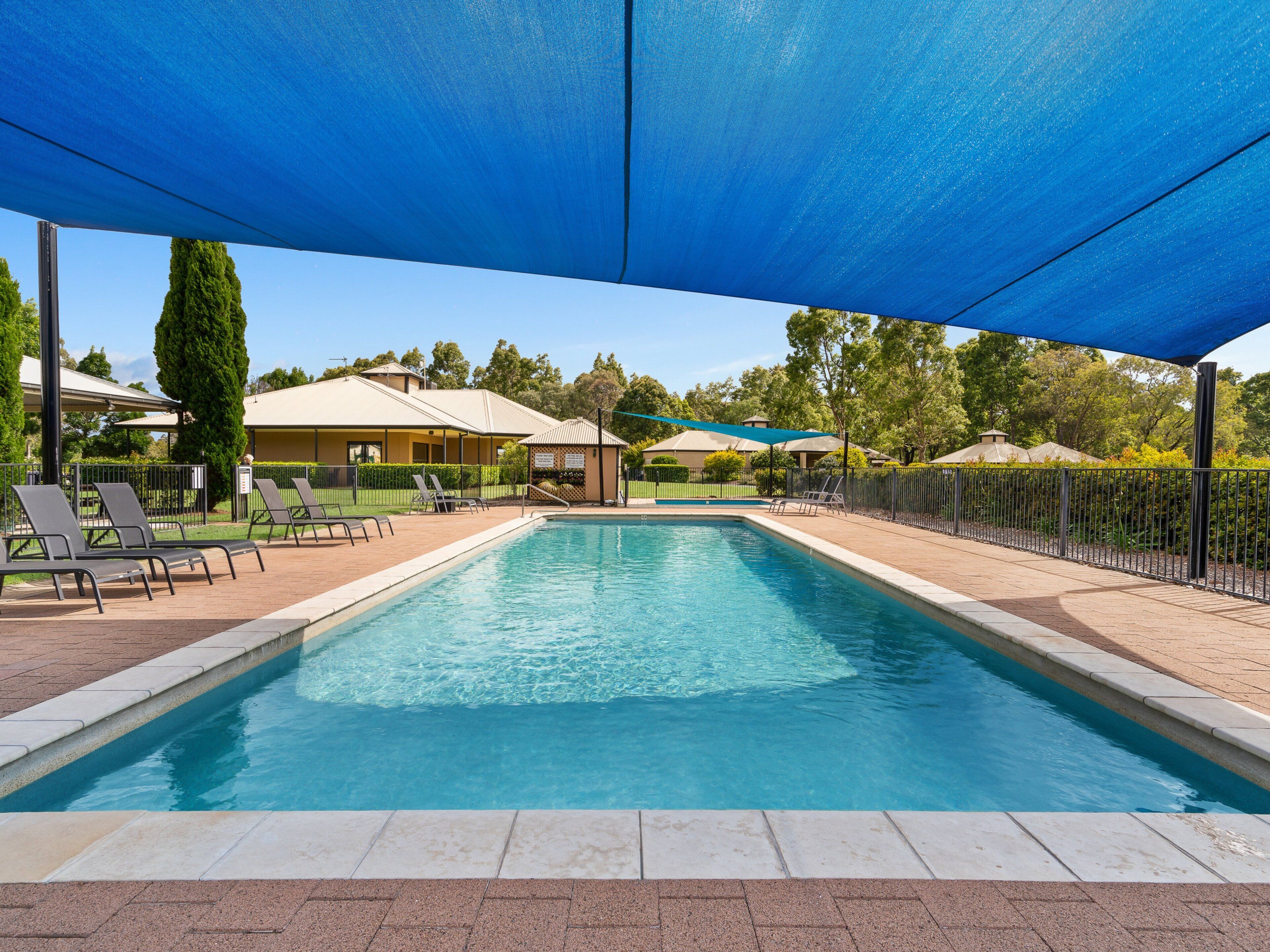Una piscina rectangular con borde de azulejos, rodeada de sillas de descanso y una zona sombreada.