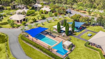 An aerial view of a resort with a large swimming pool, multiple guest villas, and a well-maintained landscape.
