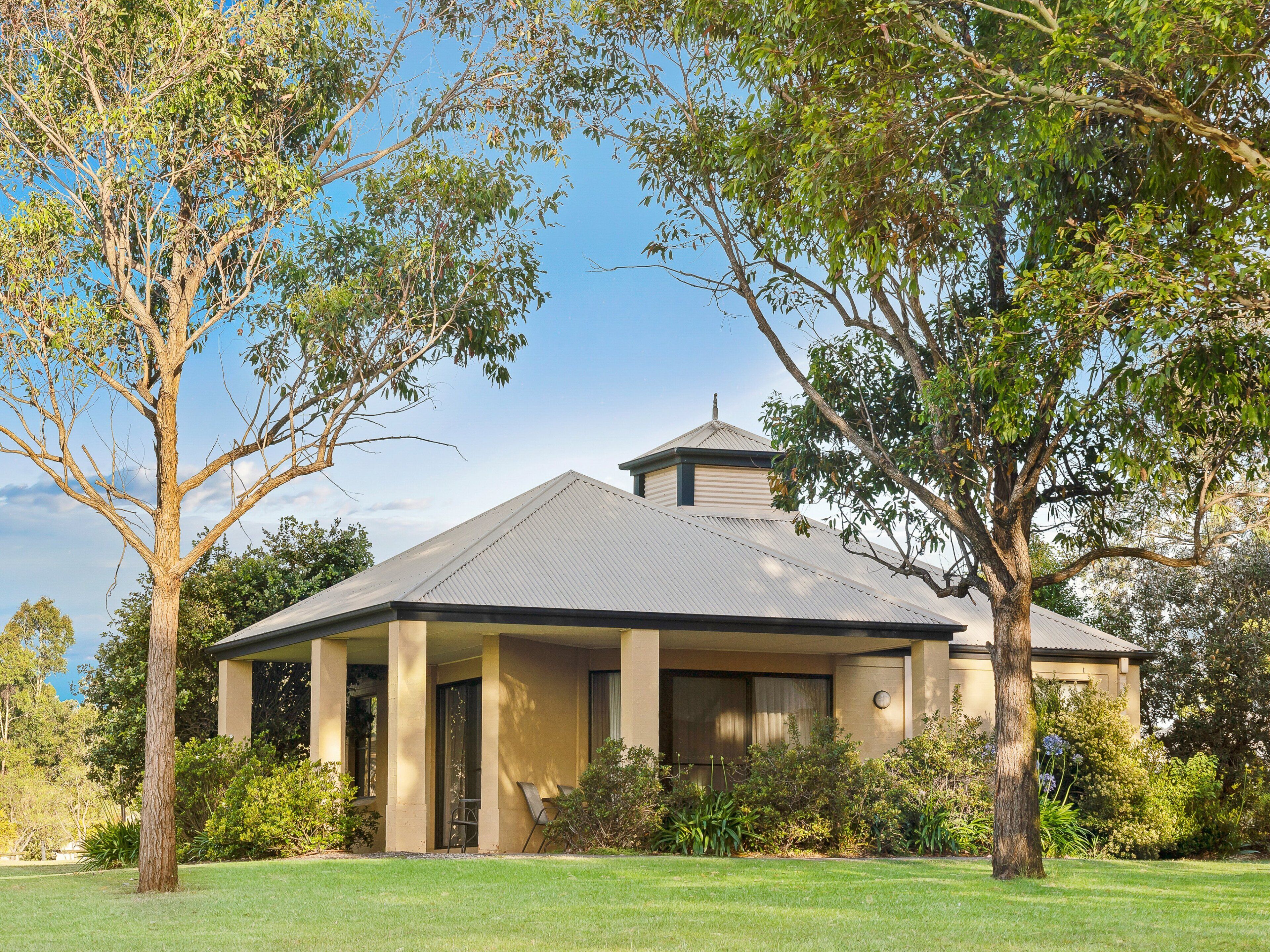 A single-story building with a gabled roof, surrounded by mature trees and a well-maintained lawn.