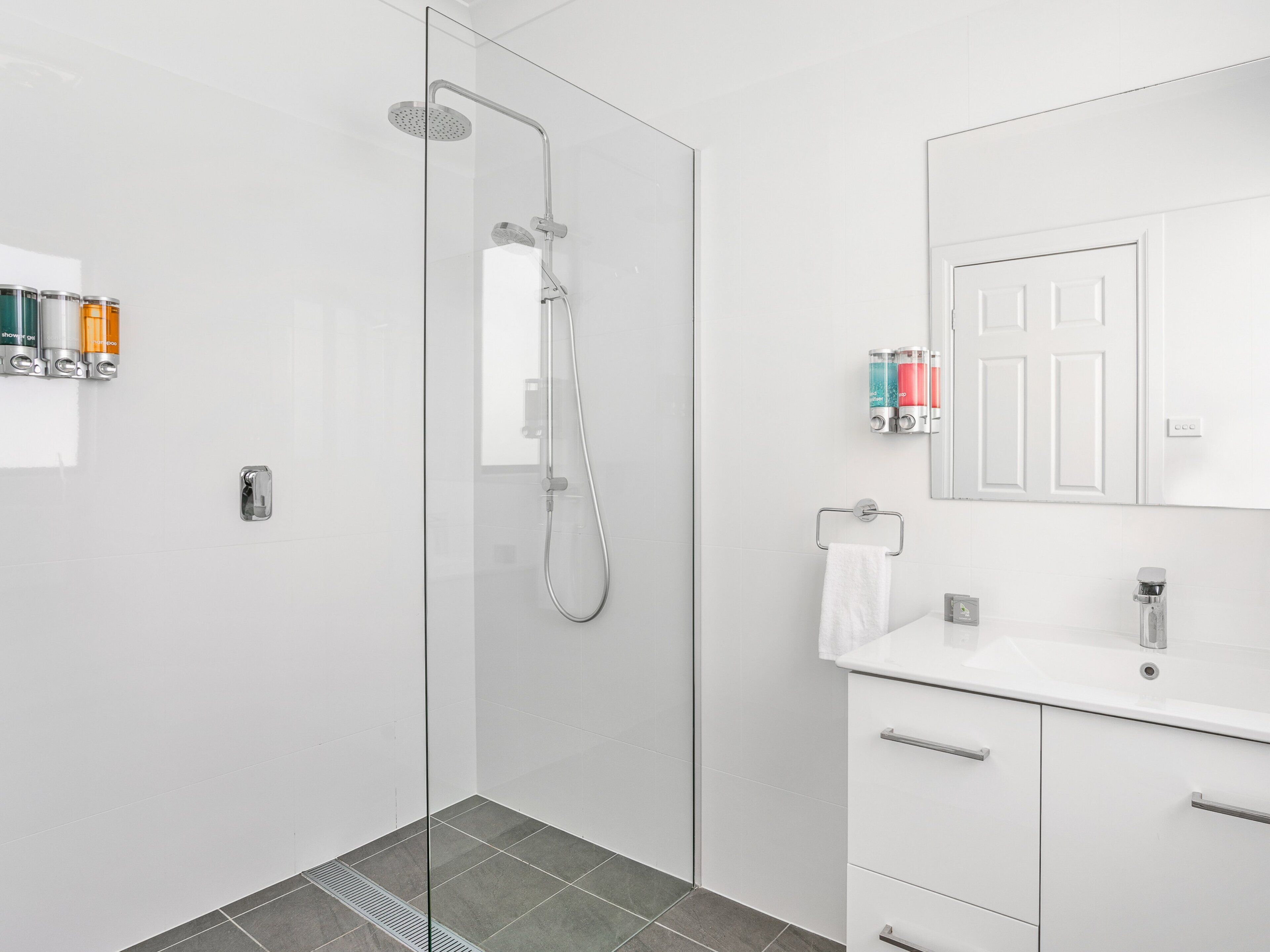 Un baño moderno con cabina de ducha de vidrio, un lavabo blanco con espejo y artículos de tocador en la pared.