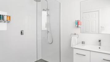 Un baño moderno con cabina de ducha de vidrio, un lavabo blanco con espejo y artículos de tocador en la pared.