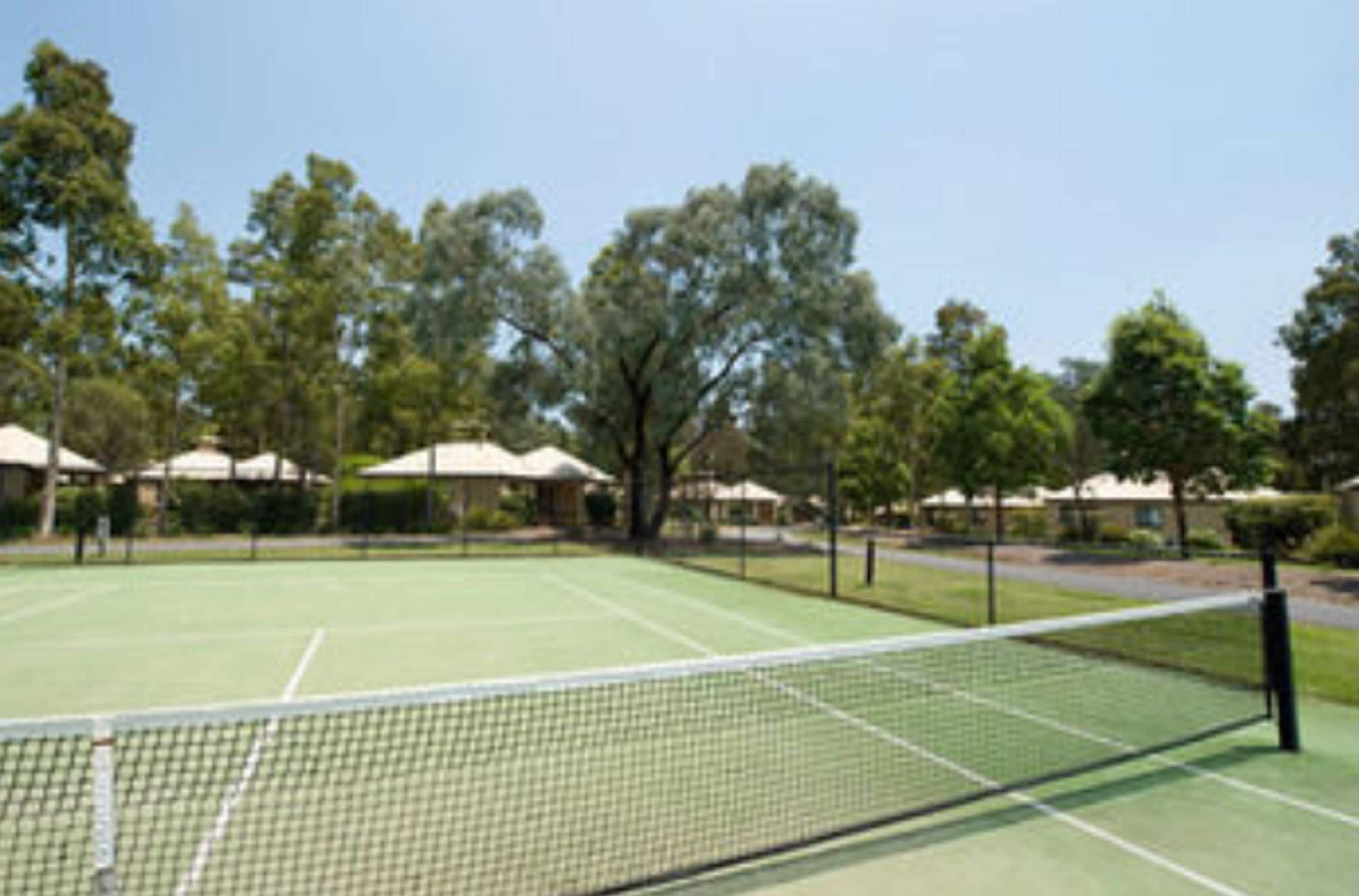 Una cancha de tenis con red, rodeada de árboles y edificios.